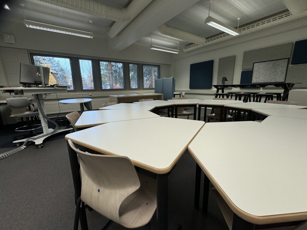 Kuva Itä-Suomen yliopiston harjoittelukoulun lukion uudistetusta oppimisympäristöstä. Kuvassa on kalusteita mm. pöytiä, tuoleja ja akustiikkalevyjä.