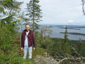 Man standing on top of a hill with trees and a lake on the background.