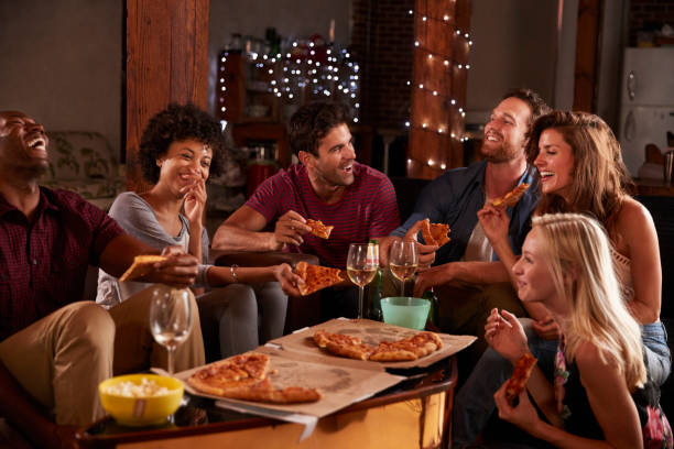 Joukko nuoria aikuisia syömässä pitsaa ja juomassa viiniä