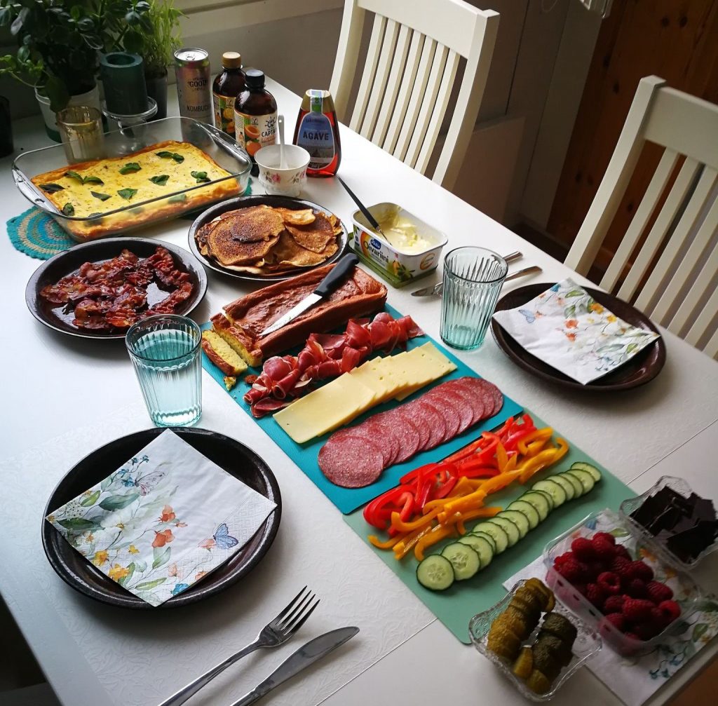 Pöytä, jossa tarjolla erilaisia ruokia kuten vihanneksia, leikkeleitä, lettuja, pekonia ja juomia