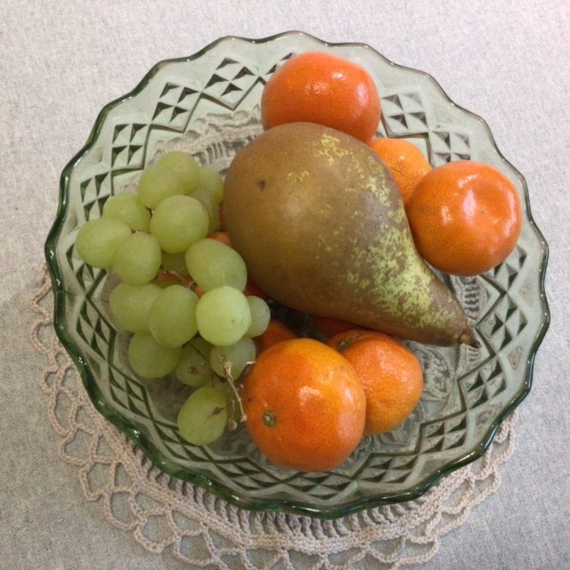 Lasikulho, jossa on mandariineja, viinirypäleitä ja päärynä