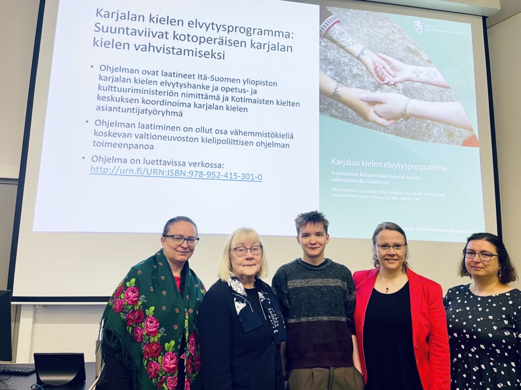Karjalan kielen opettajia ja elvytysohjelman kirjoittajia seisoo ohjelmaa käsittelevän diaesityksen edessä