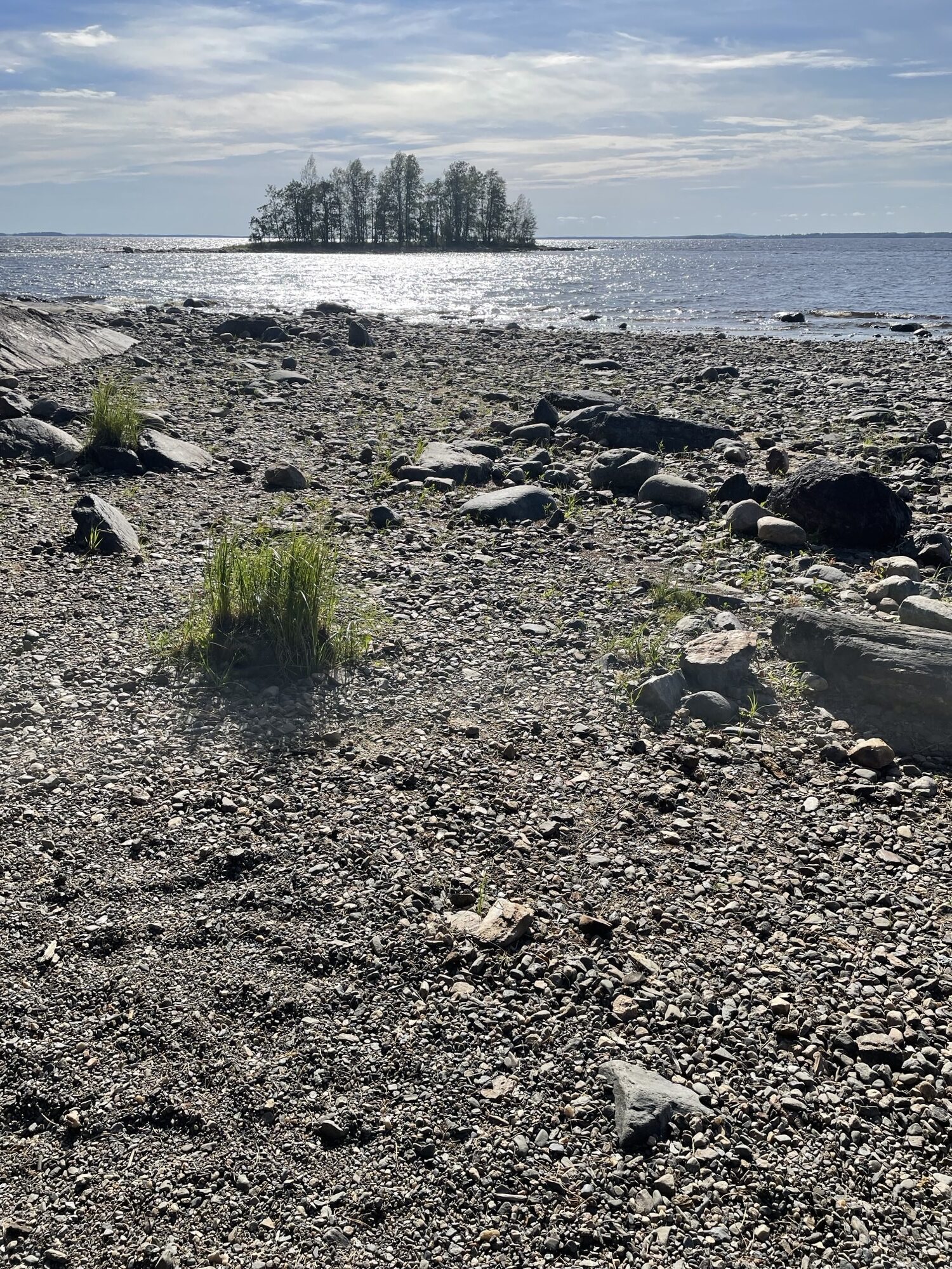 kivinen ranta, taustalla pieni saari, jossa kasvaa muutamia puita