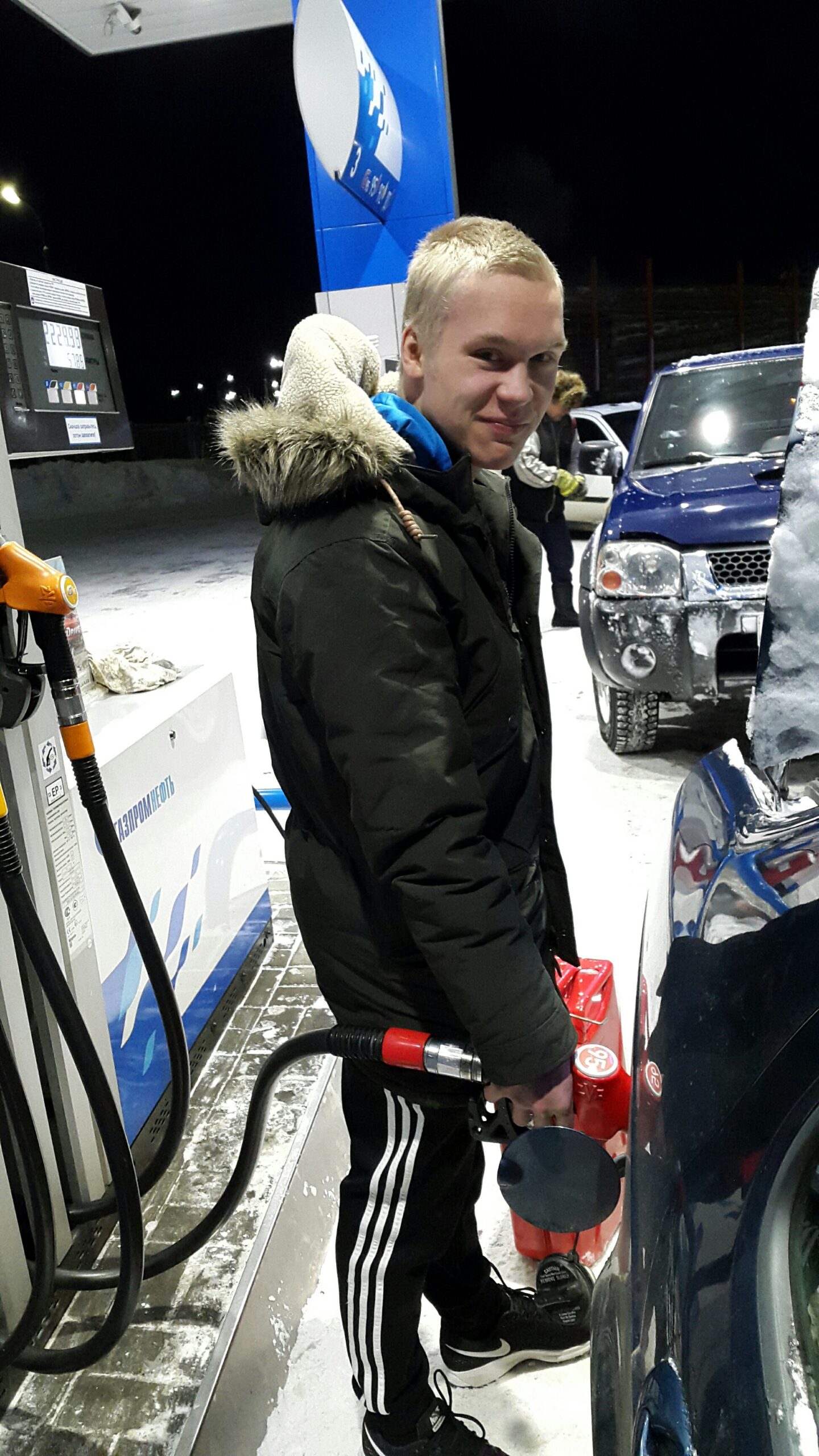 Nuori mies tankkamassa autonsa. Takana jono.