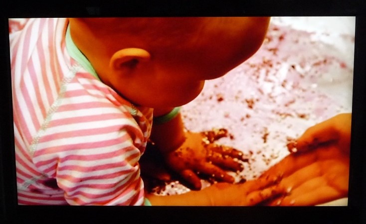 Vauvan värikylpy. Vauva levittelee käsillään värjäävää ainetta alustaan.