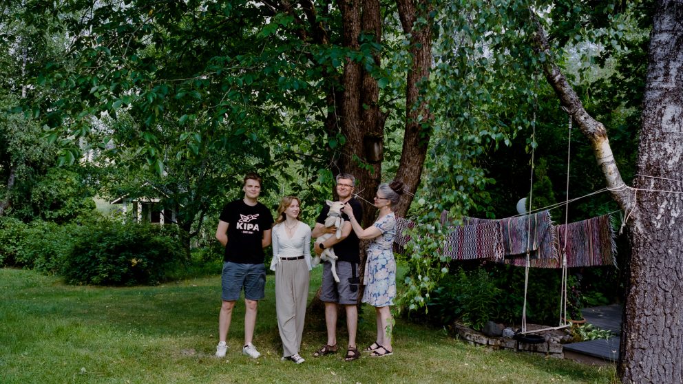Perhe kuvattu kotipihallaan puun edessä.