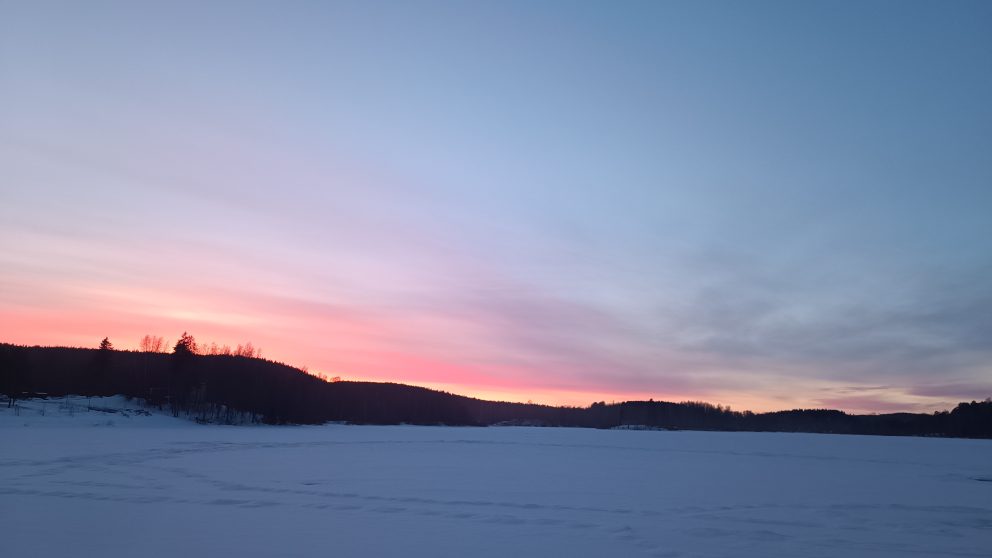 Vaaleanpunainen auringonlasku talvisen järven takana.