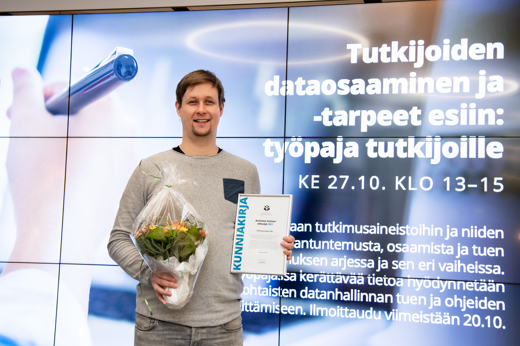 Mies, jolla käsissä kukkakimppu ja kunniakirja. Man holding a buquet of flowers and certificate of award.