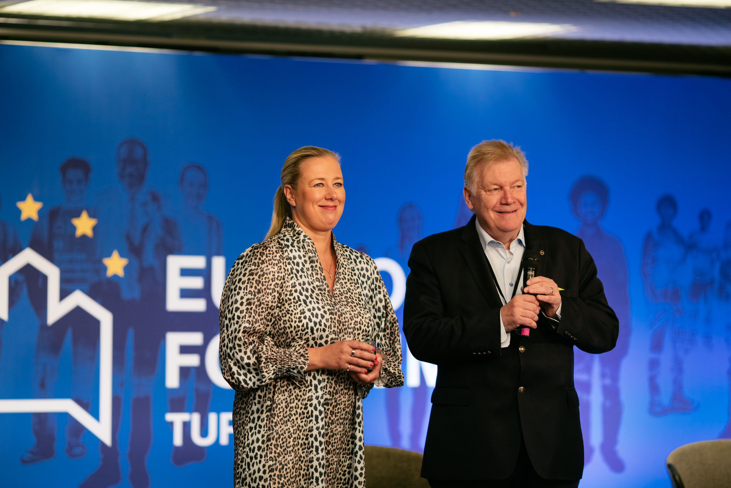 Jutta Urpilainen ja Anders Blom Eurooppa-foorumissa 2022. Kaksi hymyilevää ihmistä lavalla.
