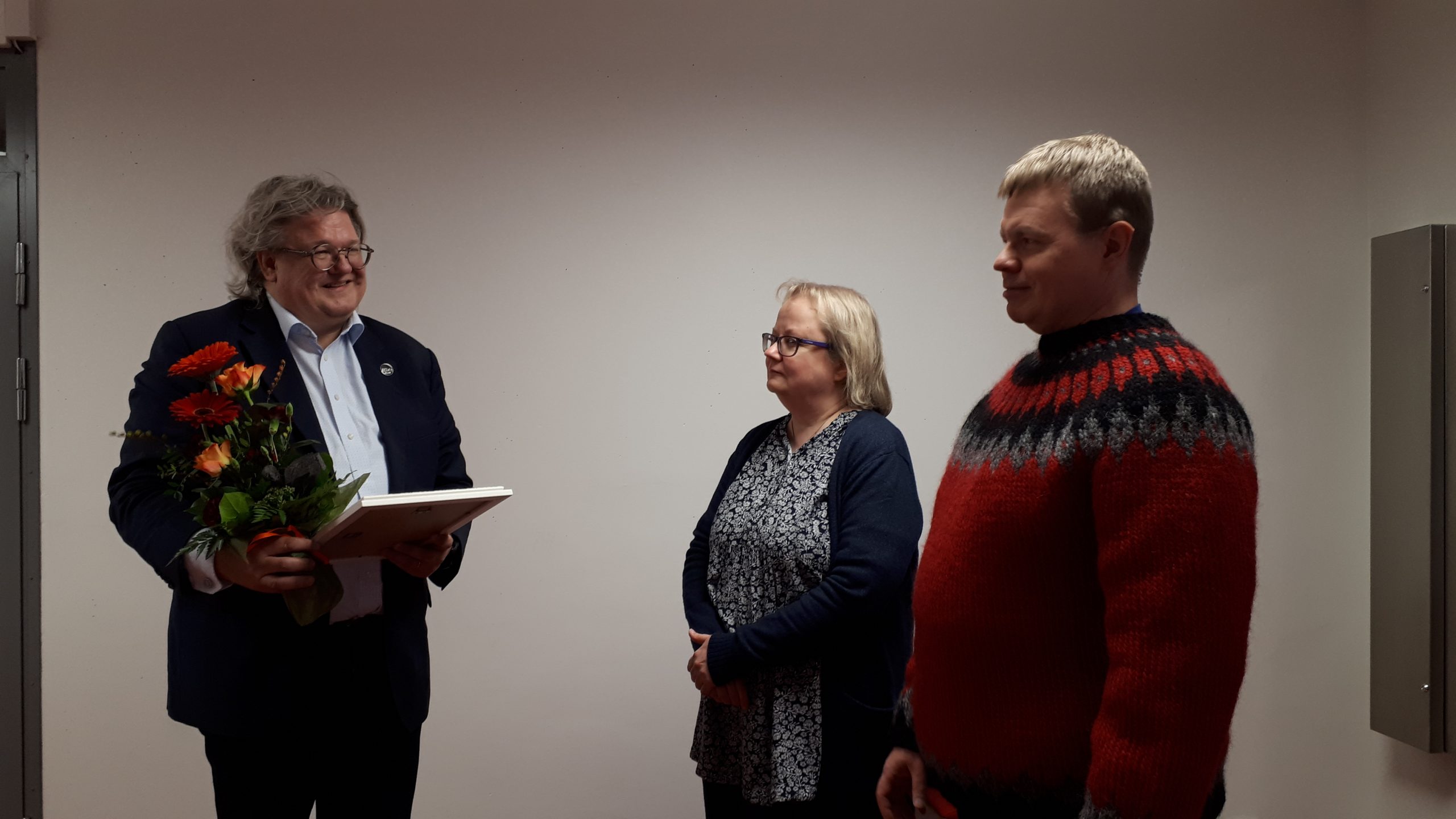 kolme ihmistä, kukkakimppu, kunniakirja. three people, flowers, diploma.