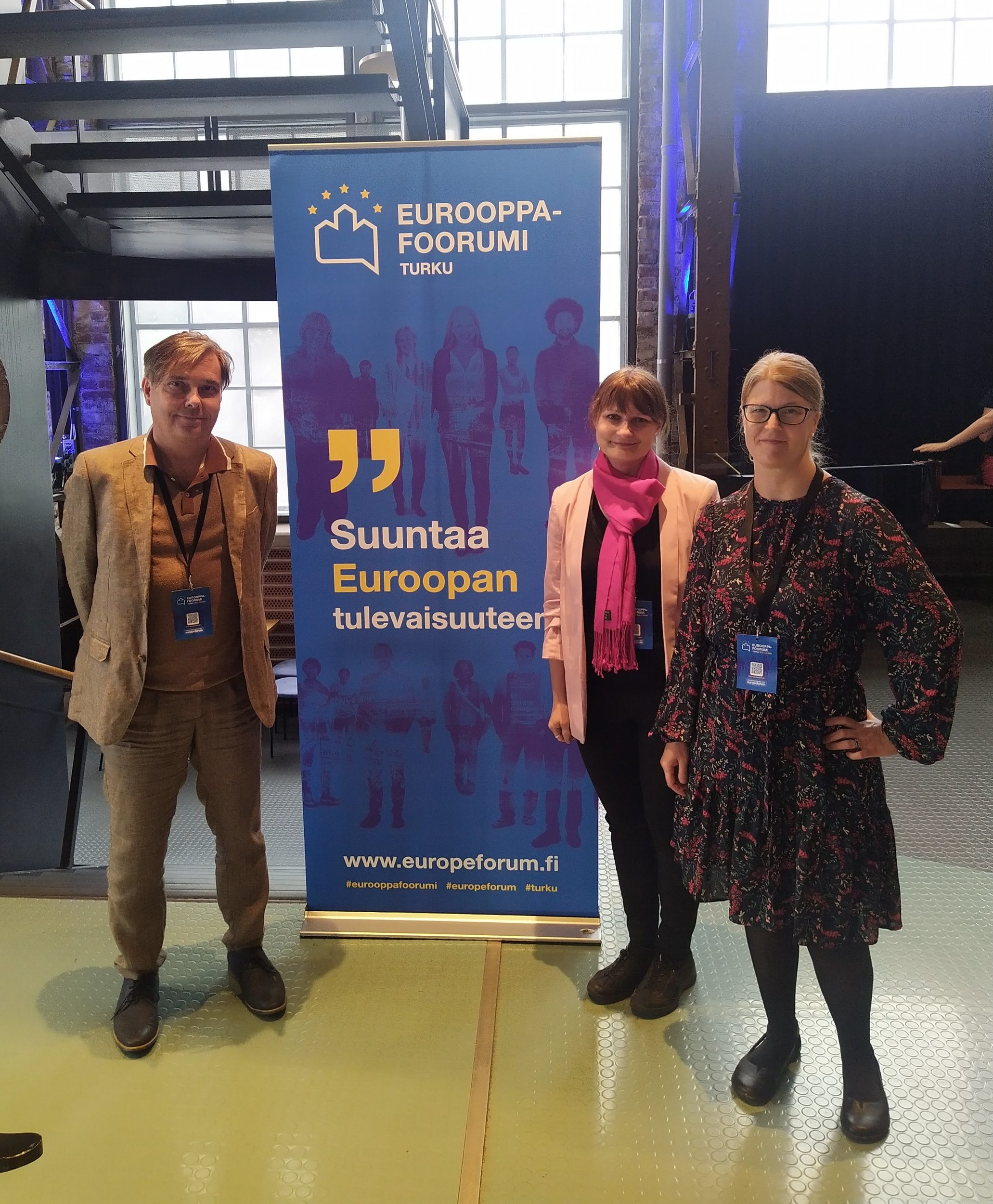 Kolme kirjastolaista Eurooppa-foorumi standin vieressä. | Three librarians next to the Europe Forum stand.