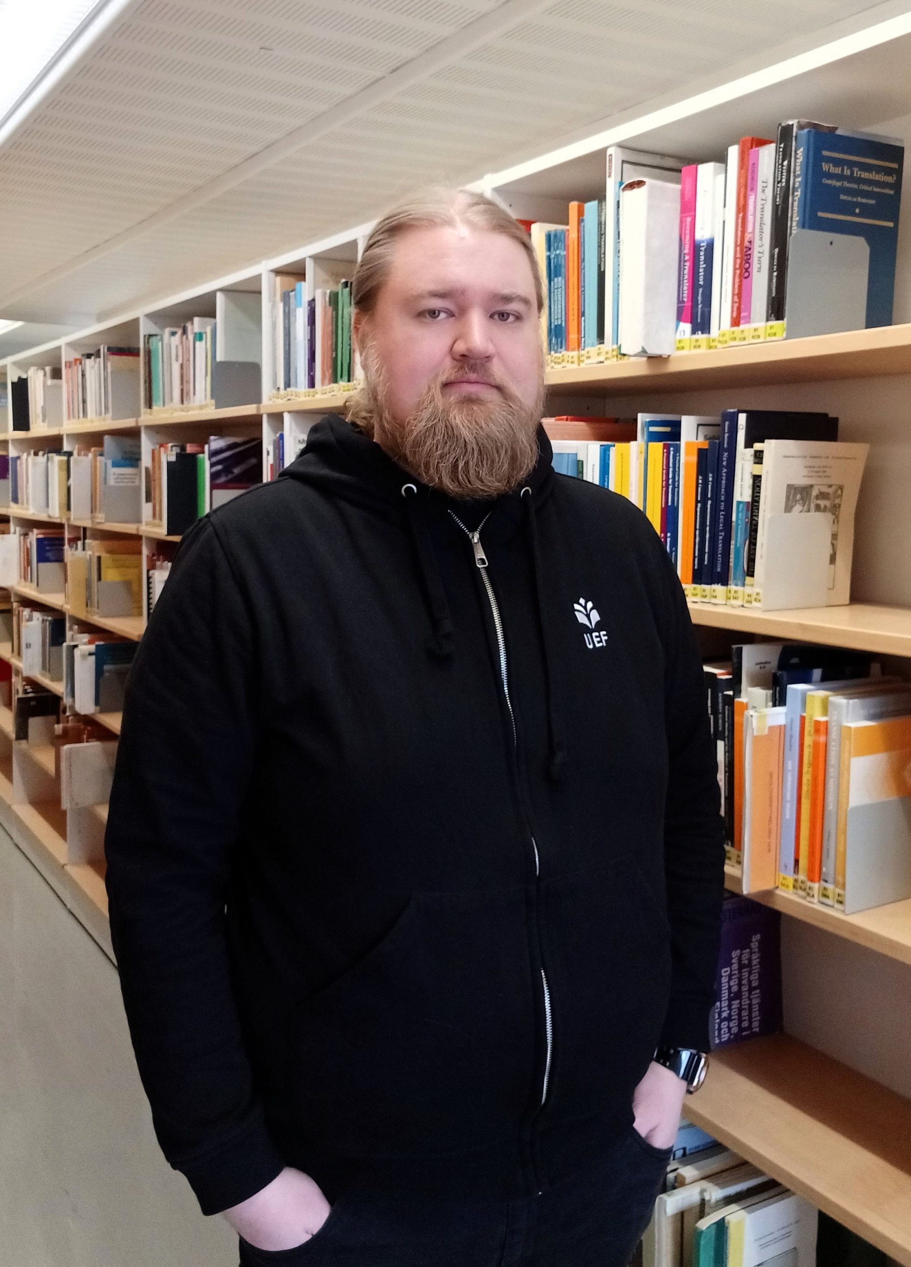 Kirjaston uusi työntekijä kirjahyllyn vieressä. LIbrary's new staff member in front of a book shelf.