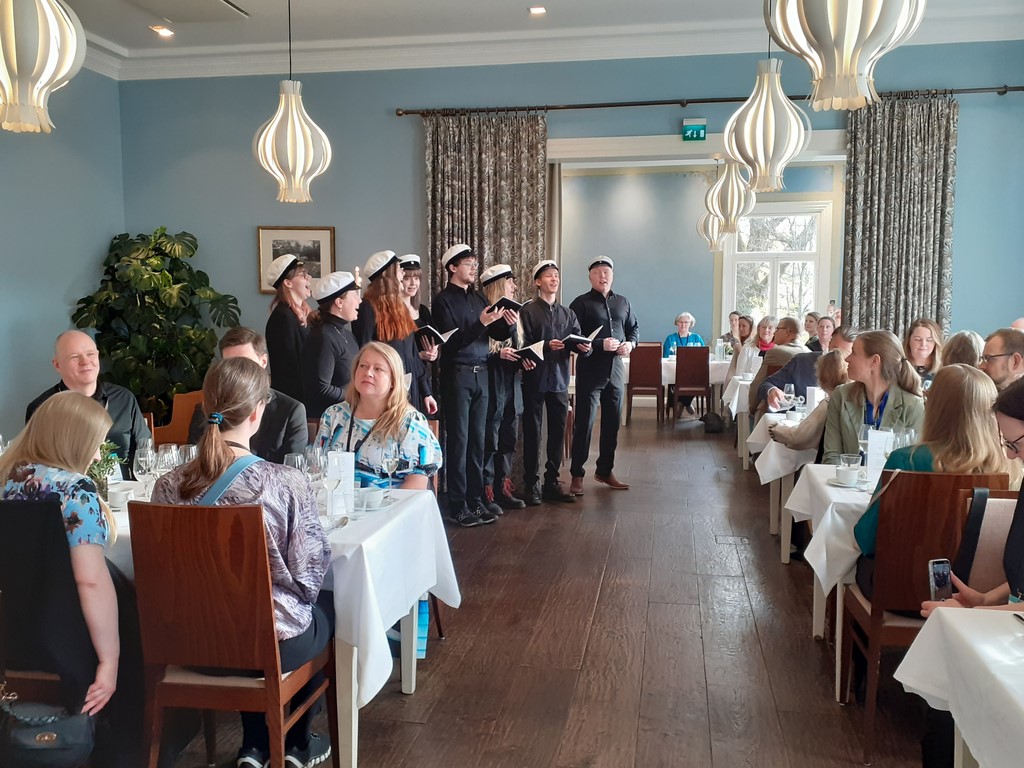 Turun yliopiston opiskelijakuoro esiintyy konferenssiosallistujille ravintolassa. Student choir of the Turku University singing to the conference participants in a restaurant.