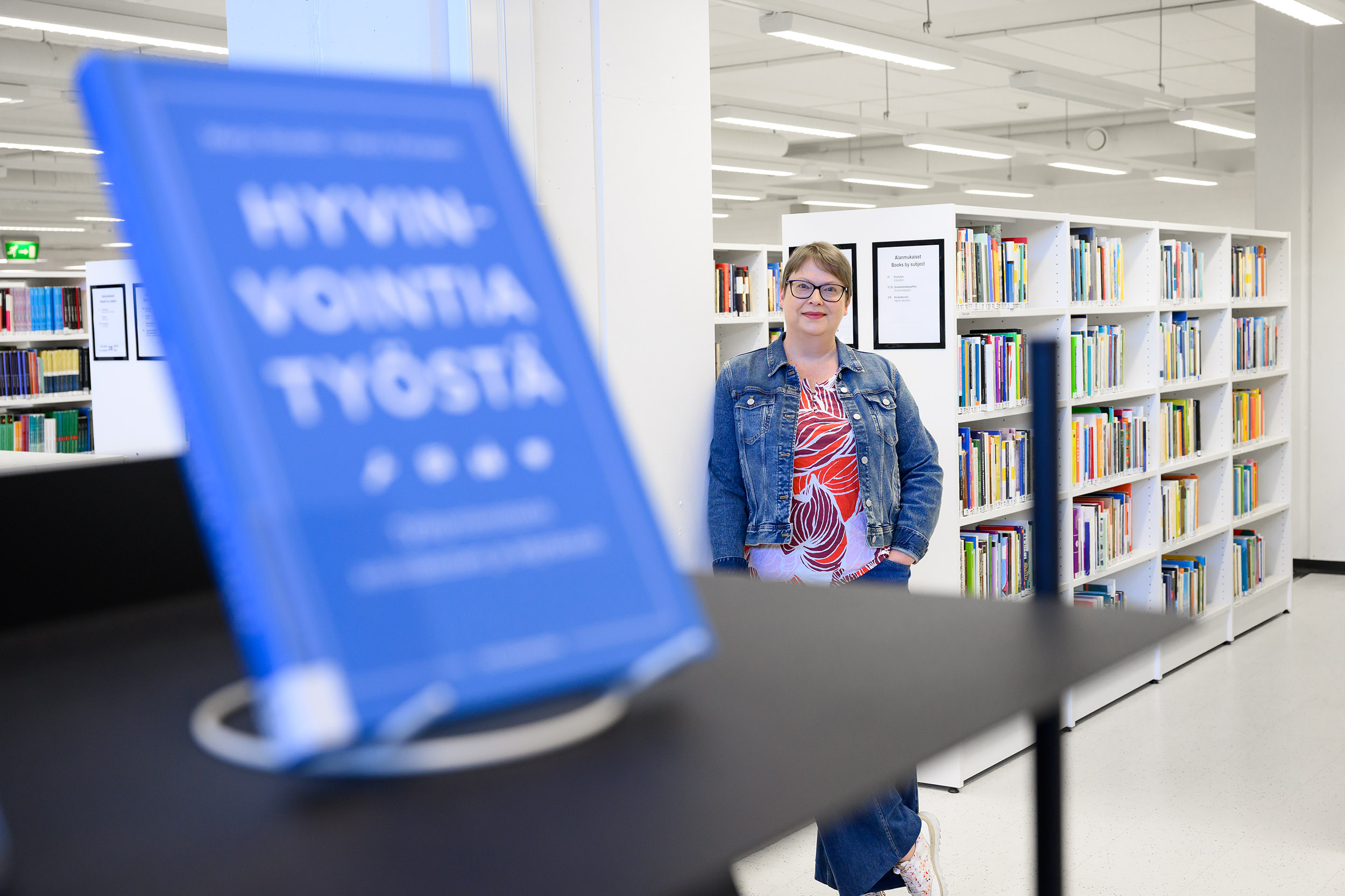 Itä-Suomen yliopiston kirjaston johtaja Irene Ylönen Kuopion kampuskirjastossa. Etualalla uutuuskirjahylly, jossa mm. kirja nimeltä Hyvinvointia työstä. The Director of UEF Library, Irene Ylönen, at the Kuopio Campus Library.