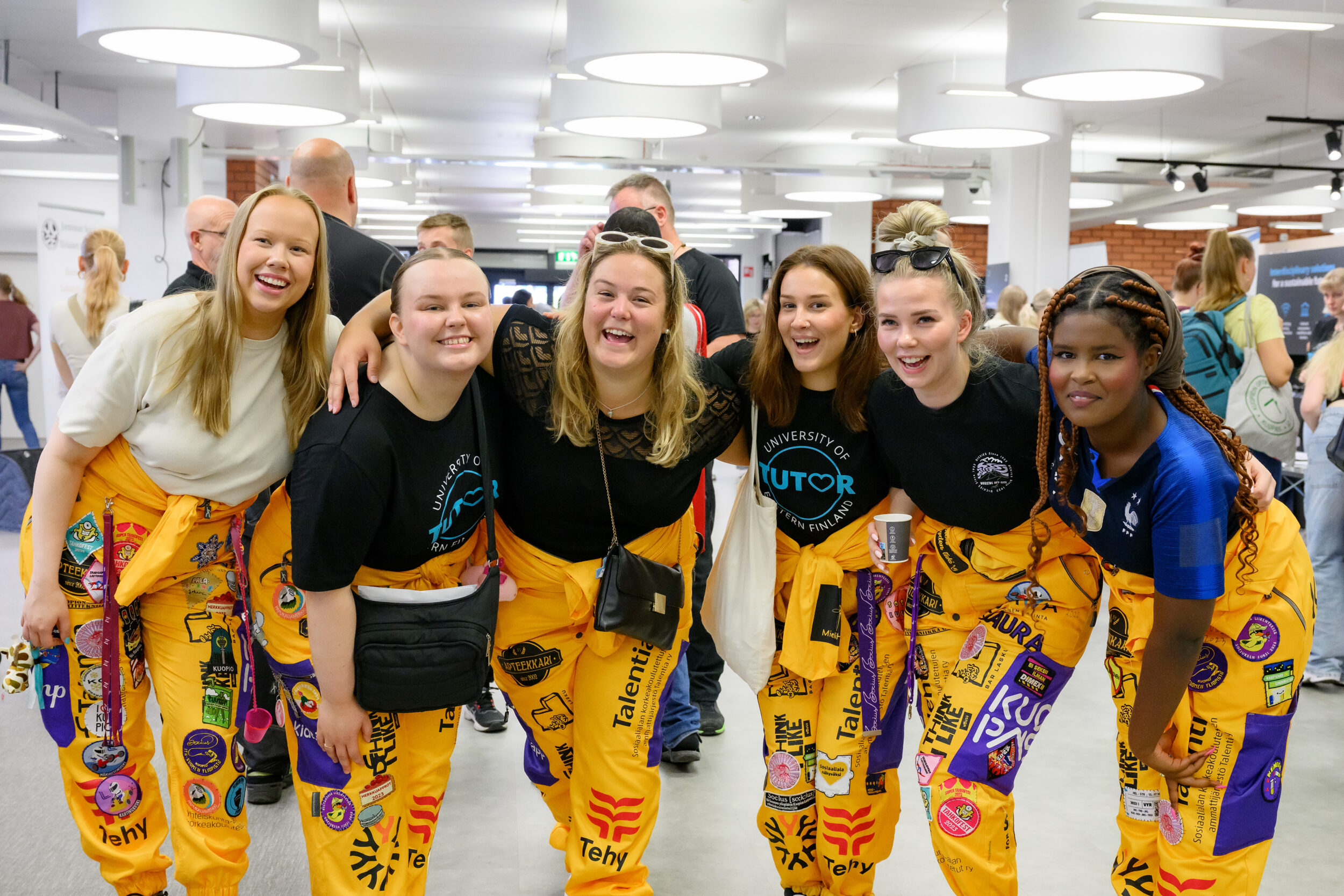 Kuusi nuorta naista kädet toistensa olalla. | Six young women with their arms around each other's shoulders.