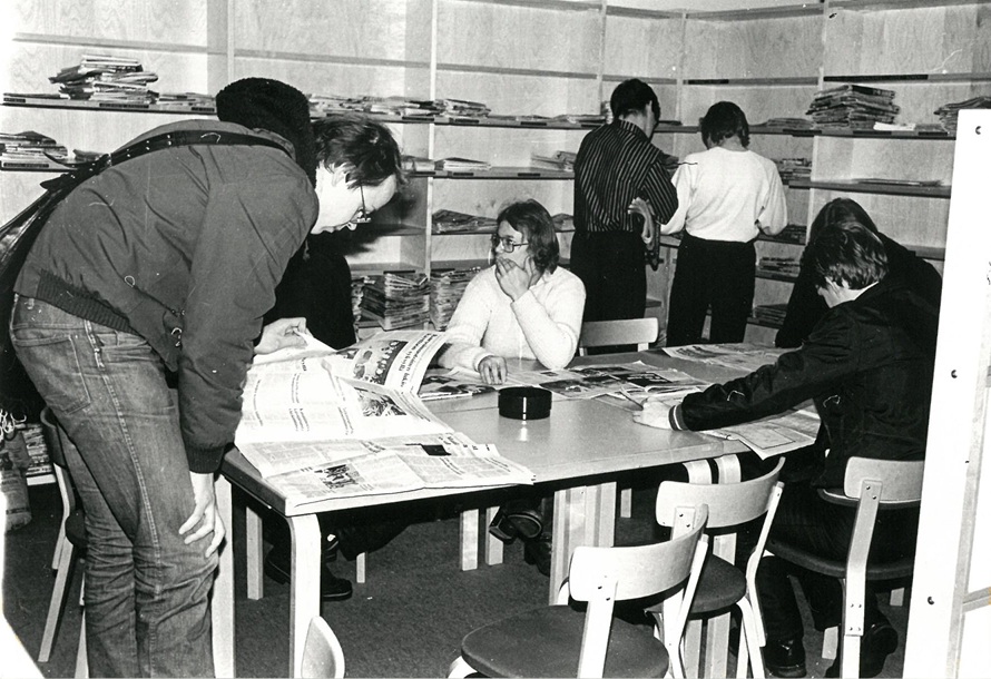 Ihmisiä lukemassa sanomalehtiä kirjastossa.