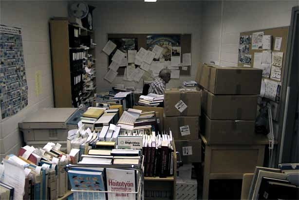 Laatikoita sekä runsaasti kirjoja kärryissä, takana mies istumassa.