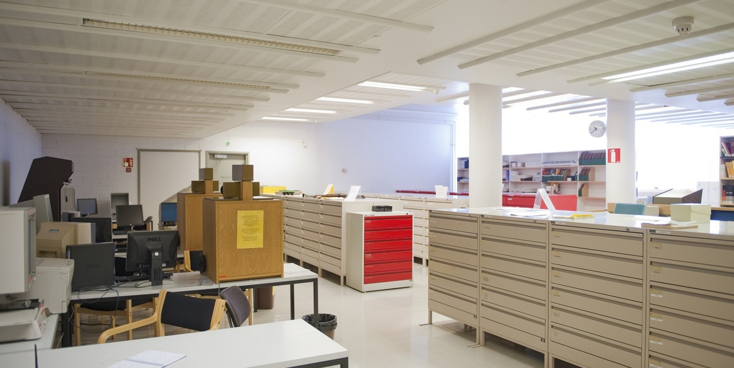 Kirjastosali jossa mikrofilmien lukulaitteita ja laatikostoja.