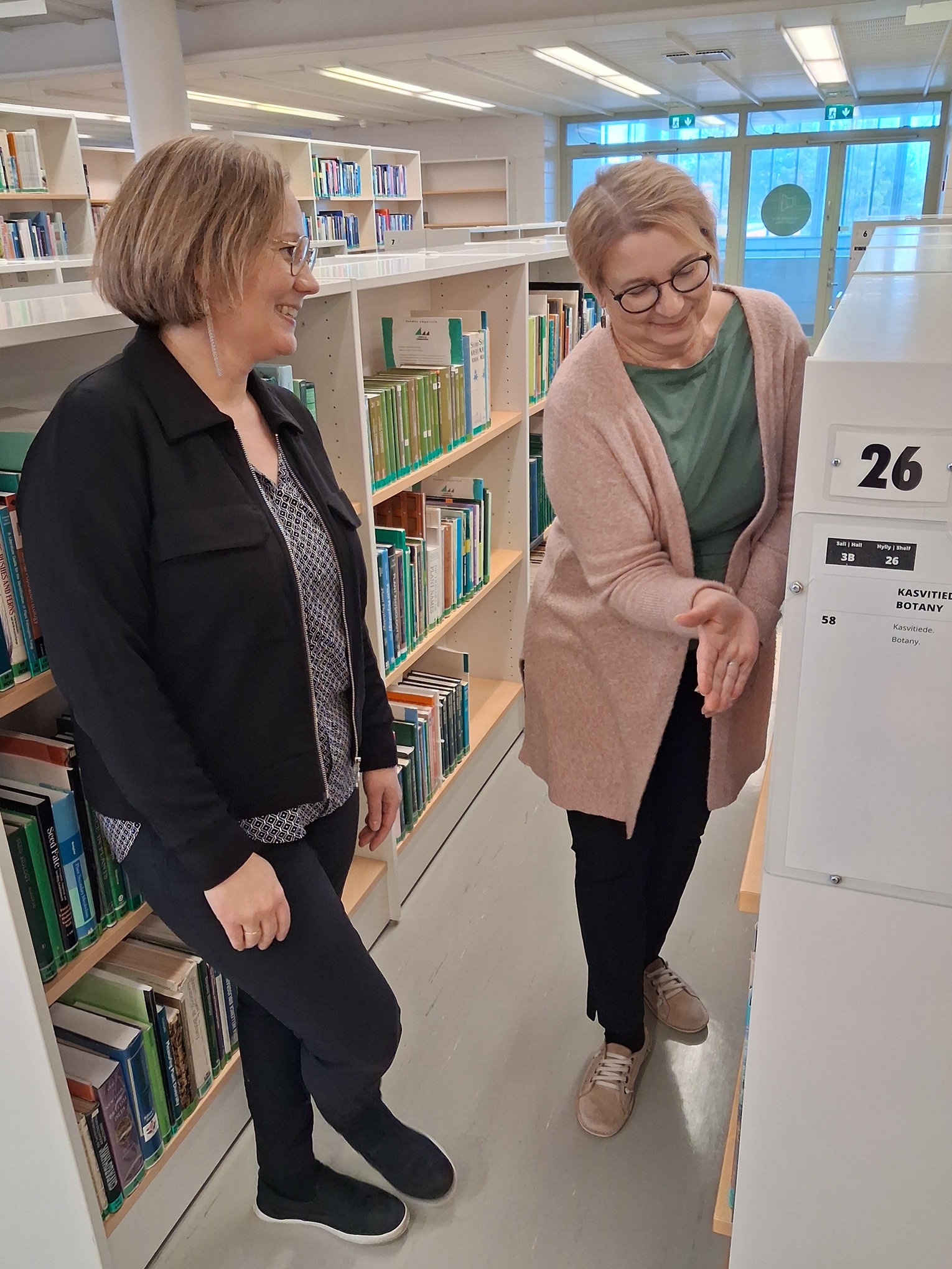 Kaksi naista seisoo kirjahyllyjen välissä.