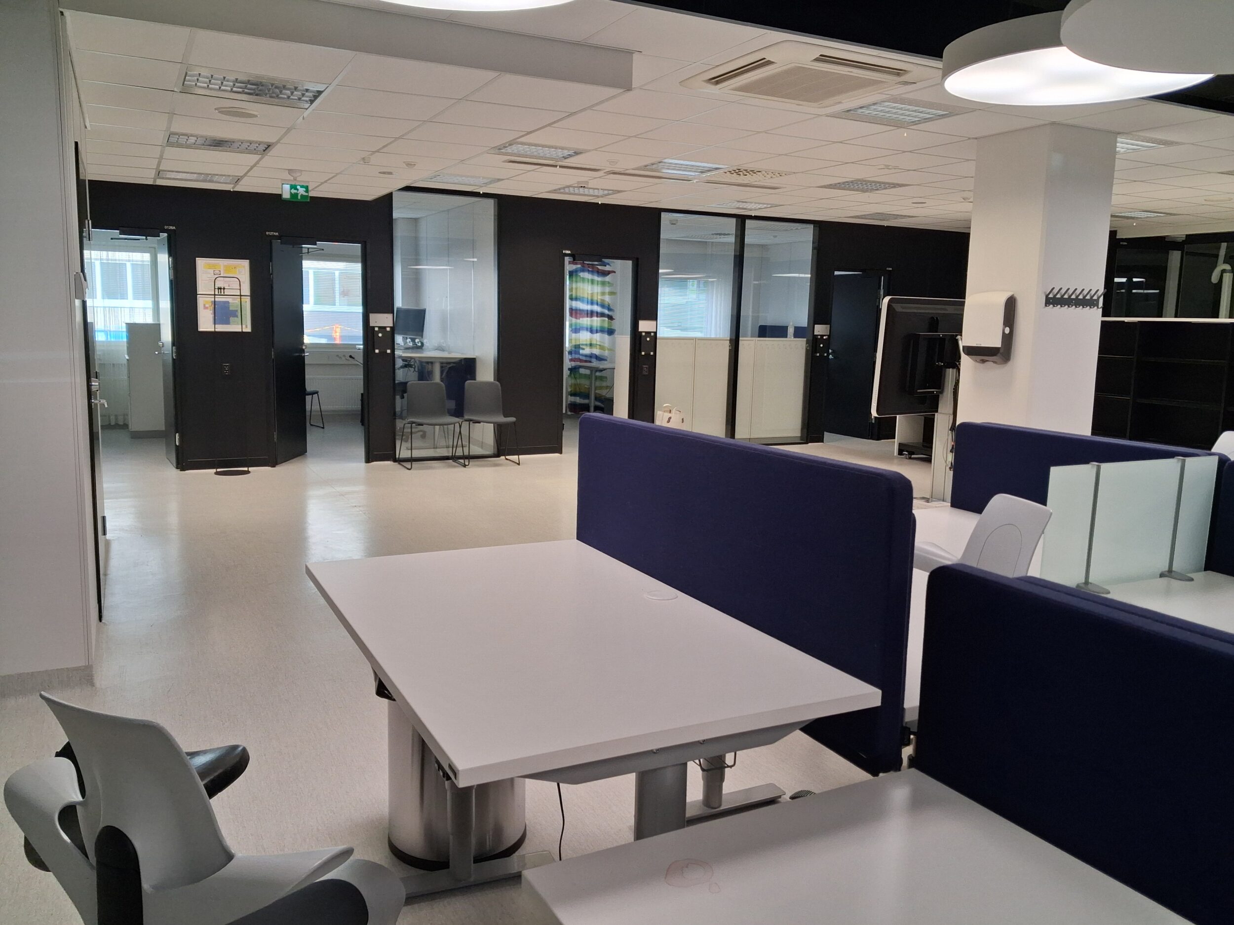 Tyhjiä työhuoneita ovet avoinna. Etualalla tyhjiä työpöytiä.
