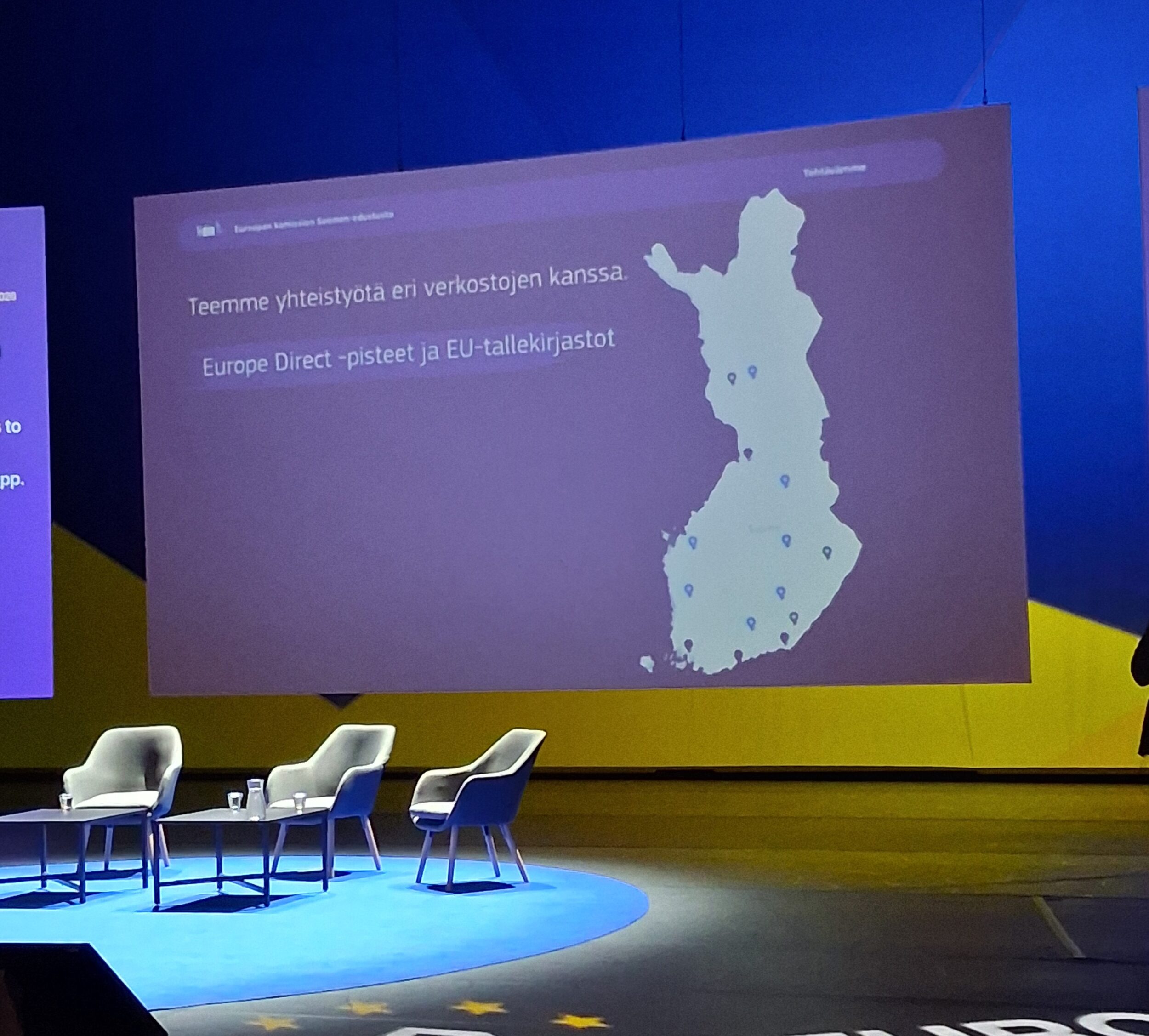 Suomen EU-tallekirjastot ja EU-Direct pisteet ovat sijoitettuna Suomen kartalle ja heijastettu suurelle valkokankaalle esiintymislavalla. | A map showing the locations of Finland’s EDC-European Documentation Centres and Europe Direct centres is projected onto a large screen on the stage.