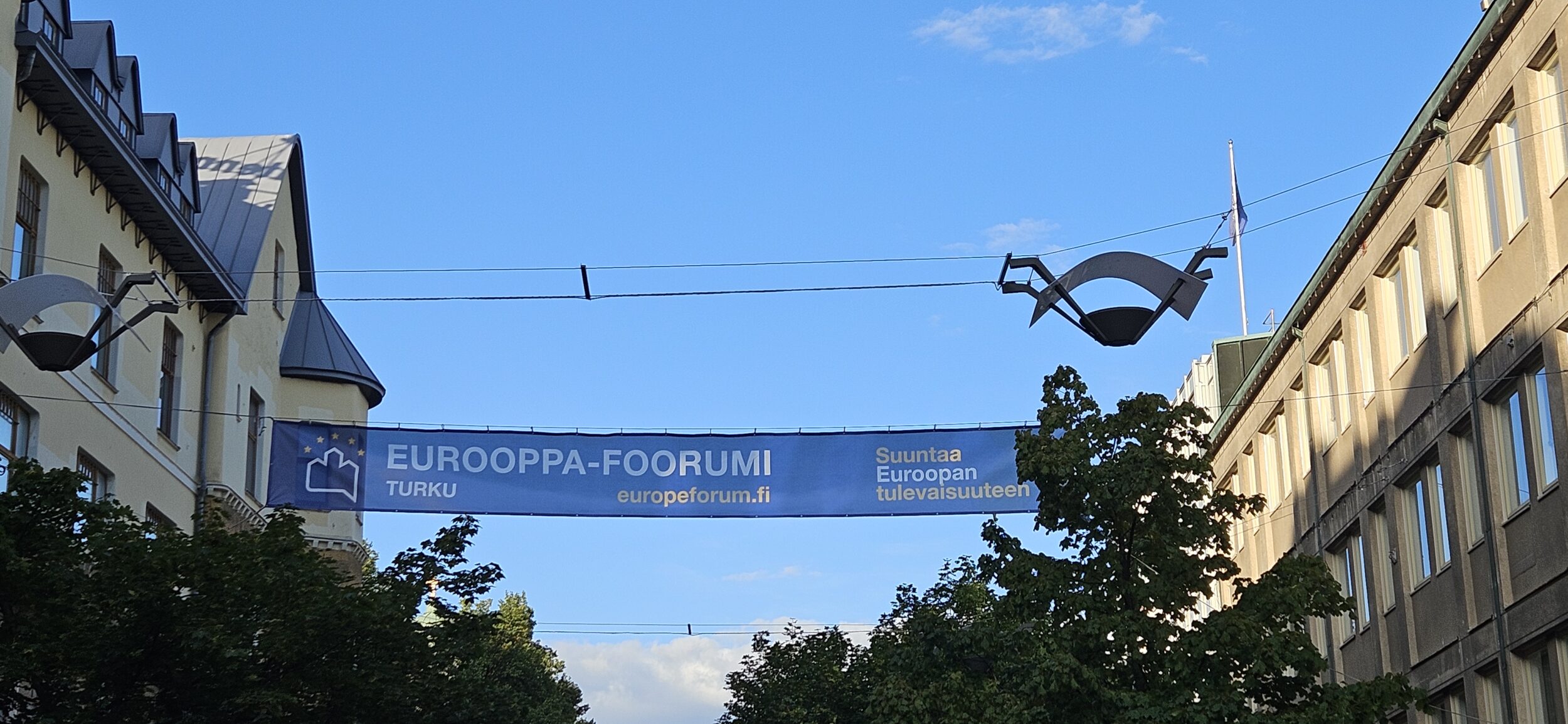 Eurooppa-foorumin mainos kadulla taivasta vasten. | A Europe Forum advertisement on a street banner against the sky.