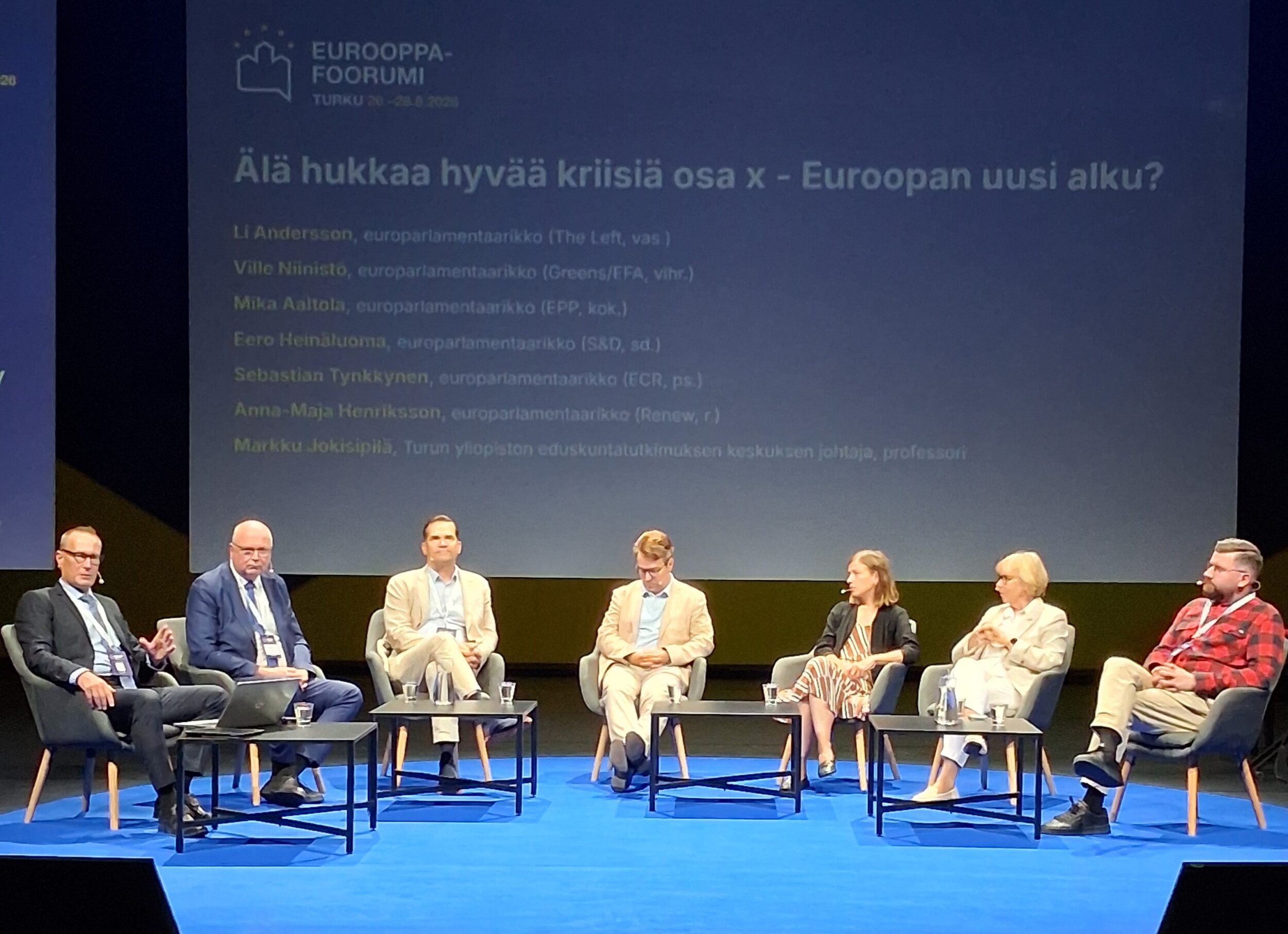 Kuusi europarlamentaarikkoa ja juontaja Eurooppa-foorumin lavalla. | Six Members of the European Parliament and the moderator on the Europe Forum stage.
