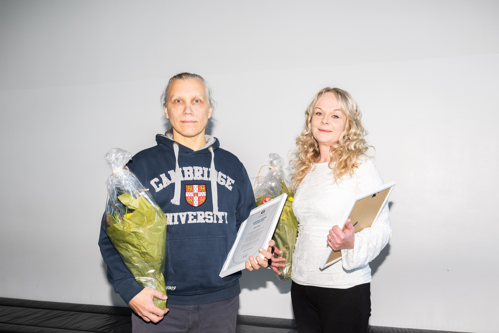 Kaksi henkilöä, joilla on käsissään kukkia ja kunniakirjat. Two people with flowers and certificates of honour on their hands.