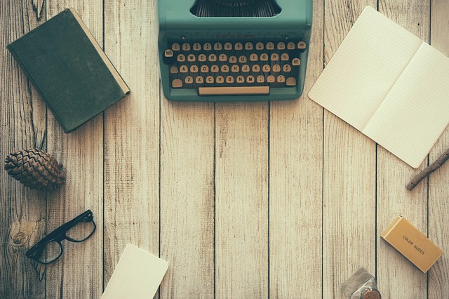 Decorative image. Typewriter, book, notebook, glasses, paper on a wooden desk.